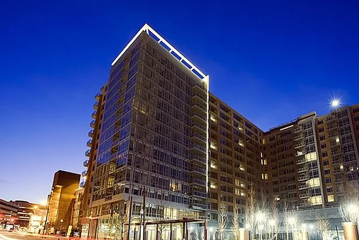 Modern high-rise apartment building illuminated at night, featuring sleek glass windows and contemporary architecture.