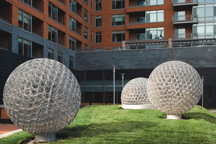Modern apartment exterior with artistic metal sculptures on lush green lawn, showcasing contemporary architectural design.
