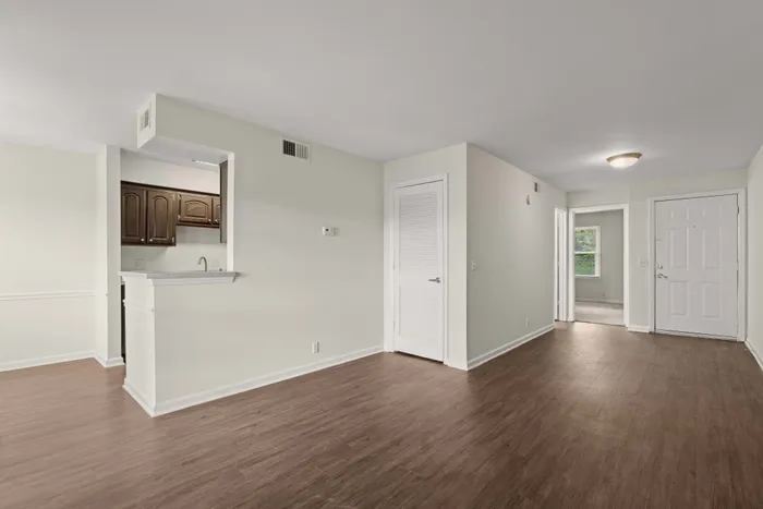 Bright and spacious apartment showcasing elegant wood flooring, a cozy kitchen nook with dark wooden cabinets, and a well-lit hallway leading to comfortable living spaces.