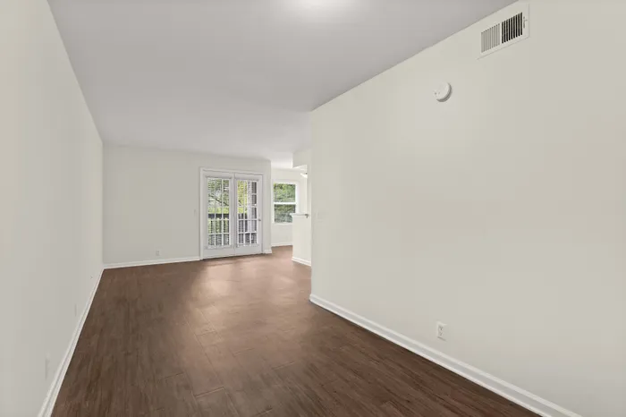 Inviting open floor plan with elegant hardwood flooring, large windows, and French doors leading to a bright outdoor view.