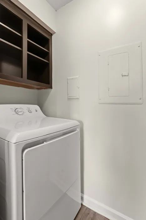 Modern laundry area featuring a sleek white dryer, complemented by open wooden shelves for storage.