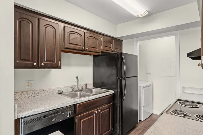 Modern kitchen with sleek dark wood cabinetry, stainless steel sink, and spacious countertops. Includes refrigerator, stove, and in-unit laundry.