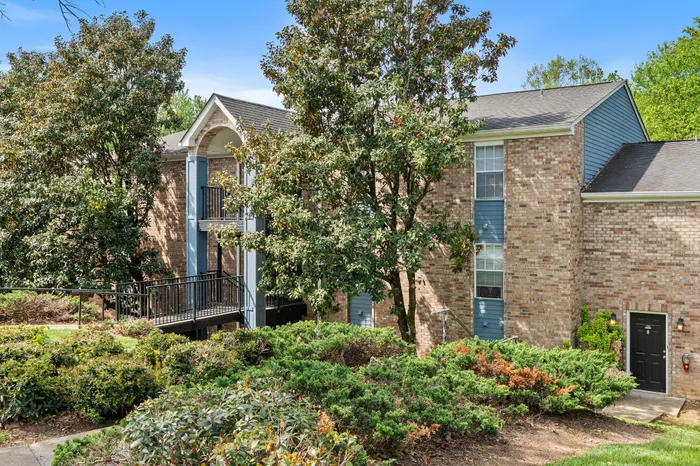 Charming brick apartment complex with lush greenery and spacious balconies, offering a serene and inviting atmosphere.