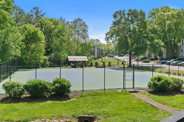 Inviting apartment complex with lush greenery, featuring a well-maintained tennis court and scenic picnic area.