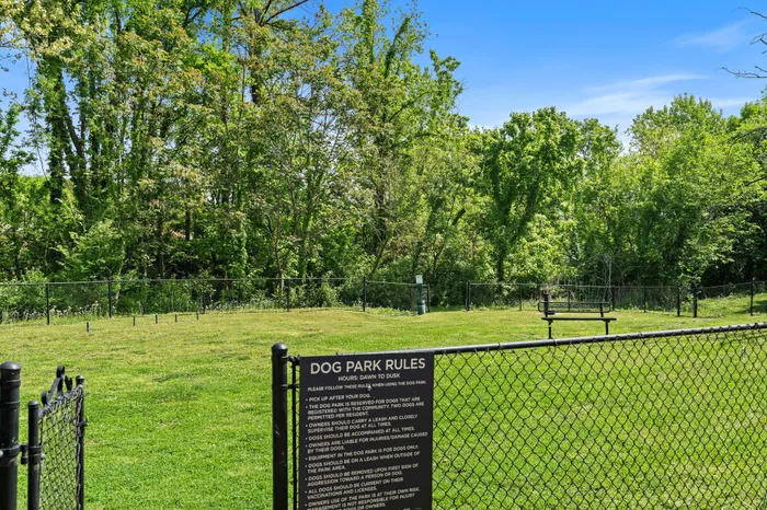 Inviting fenced dog park with lush green grass and wooded backdrop, ideal for pet-friendly community living.