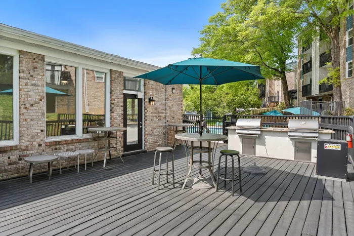 Inviting outdoor patio featuring a modern grill station, umbrella-covered seating, and lush greenery, perfect for entertaining.