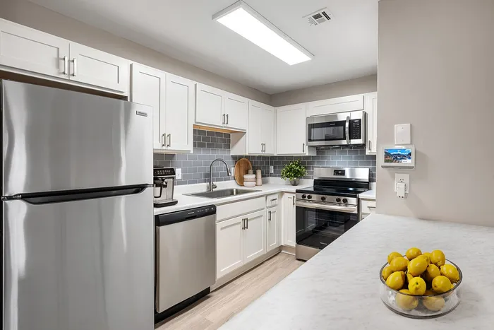 Elegant modern kitchen with stylish white cabinetry, stainless steel appliances, and a sleek countertop adorned with a bowl of lemons, creating a fresh and inviting ambiance.