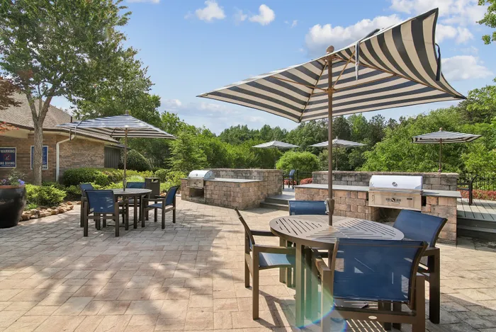Charming outdoor patio with stylish seating, sunshades, and a built-in grill, surrounded by lush greenery.