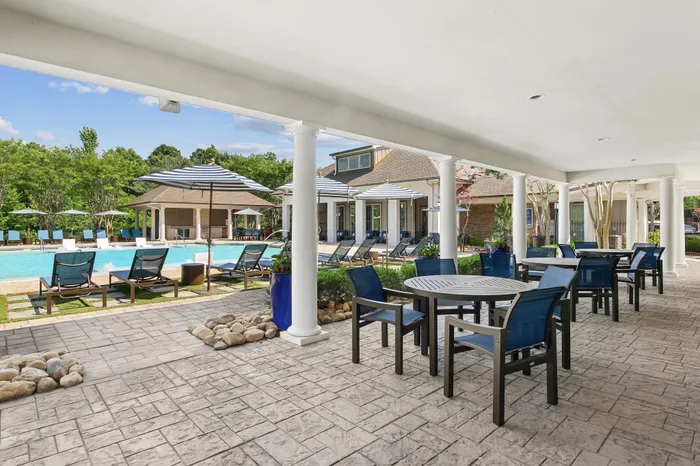 Luxurious poolside view with elegant seating area under a canopy, surrounded by lush greenery and stylish lounge chairs.