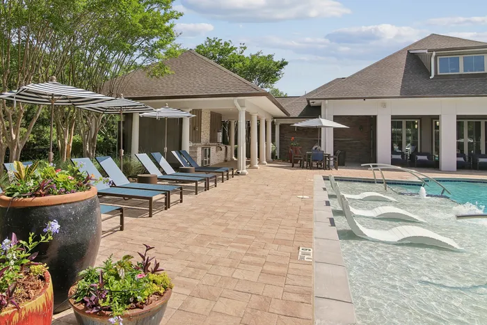 Luxurious poolside retreat with stylish lounge chairs, shaded seating areas, and vibrant potted plants under a clear blue sky.