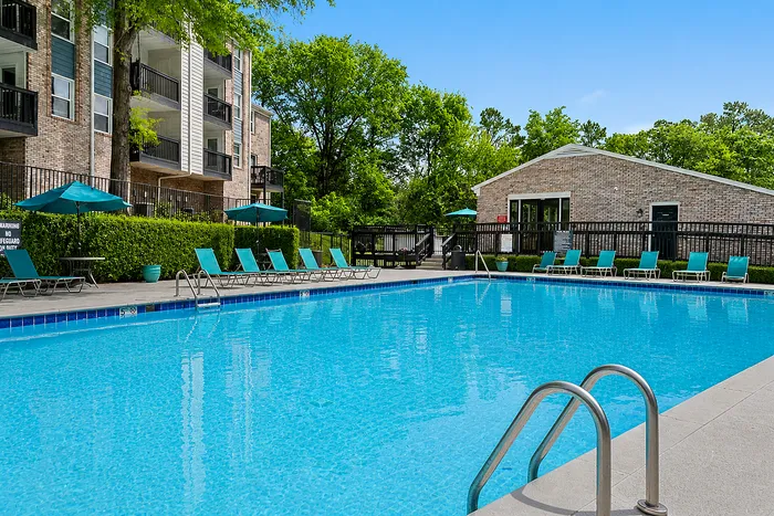 Inviting outdoor pool area with stylish lounge chairs and umbrellas, surrounded by lush greenery and modern apartment buildings.