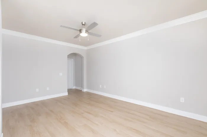 Bright and spacious room with elegant wood flooring, modern ceiling fan, and a welcoming archway.