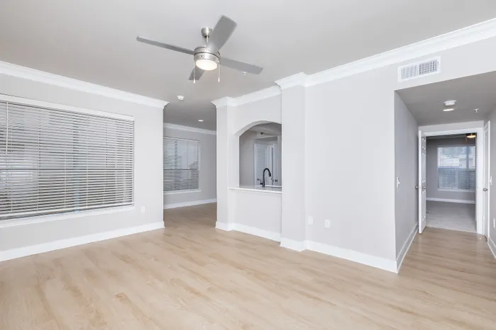 Bright open-plan living area with wood flooring, modern ceiling fan, and large windows for natural light.