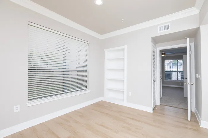 Bright room featuring elegant wood flooring, large windows with blinds, and built-in shelving, offering modern and functional living space.