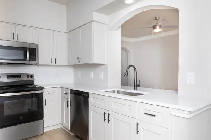 Contemporary kitchen with sleek stainless steel appliances, elegant white cabinetry, and a stylish archway.