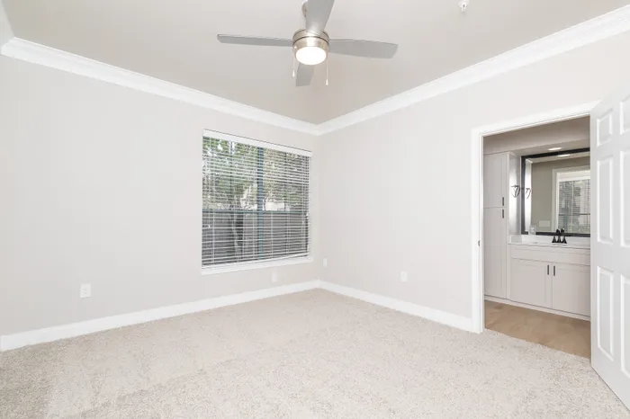 Inviting and spacious bedroom with plush carpeting, featuring large window for ample natural light and a modern ceiling fan.