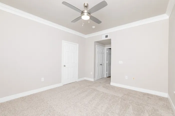 Bright and spacious bedroom with plush carpeting, featuring modern ceiling fan and pristine white doors.