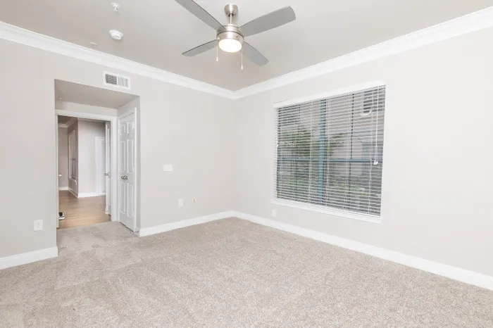 Bright and inviting bedroom with plush carpeting, modern ceiling fan, and large window offering ample natural light.