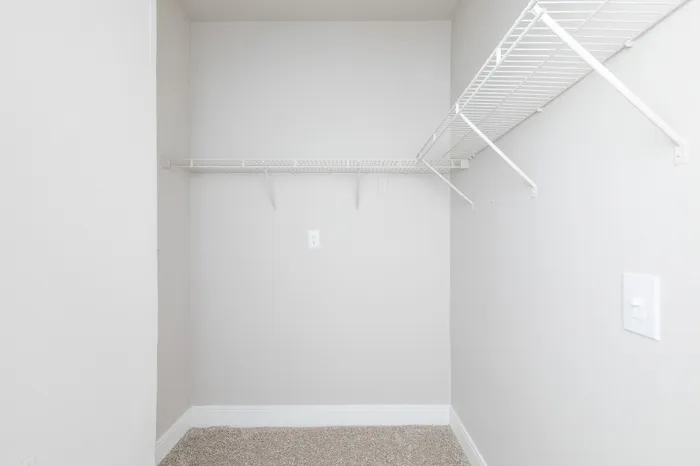 Spacious walk-in closet with ample shelving and pristine white walls, perfect for organized storage solutions.