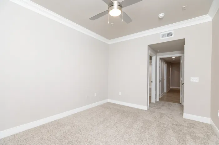 Bright and spacious bedroom with plush carpeting and modern ceiling fan, perfect for a tranquil retreat.