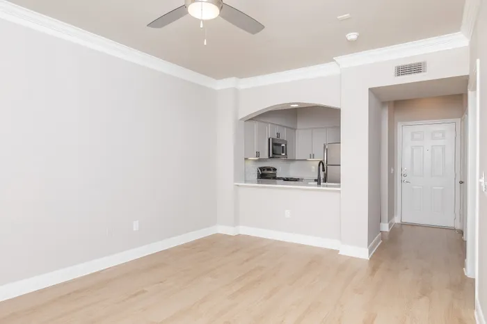 Modern apartment interior featuring a bright, open-concept living area with light wood flooring, ceiling fan, and a sleek kitchen with stainless steel appliances.
