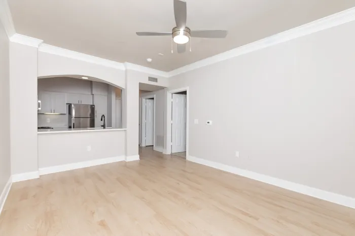 Bright, open-concept living area with sleek hardwood floors and modern ceiling fan, leading to a stylish stainless steel kitchen.