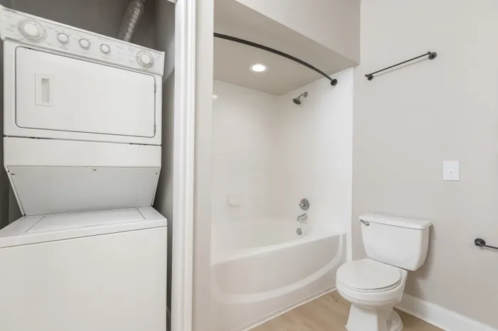 Modern bathroom with in-unit washer and dryer, featuring a full bathtub and sleek fixtures.