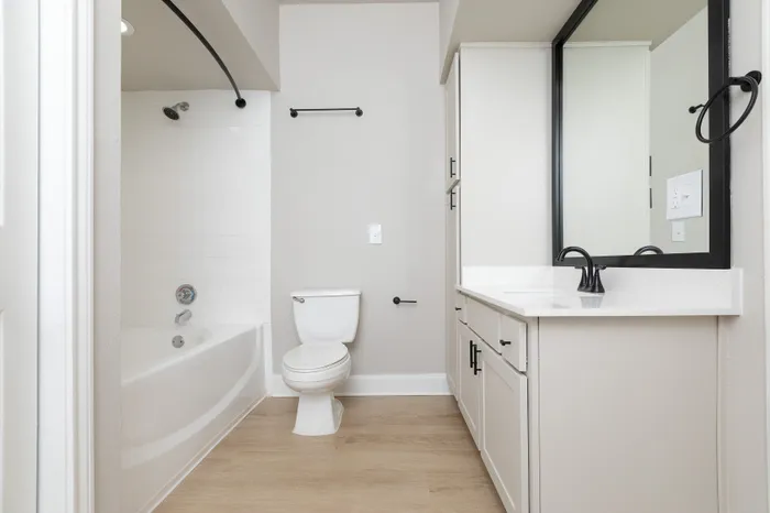 Bright and modern bathroom featuring sleek white cabinetry, a spacious mirror, and elegant black fixtures.