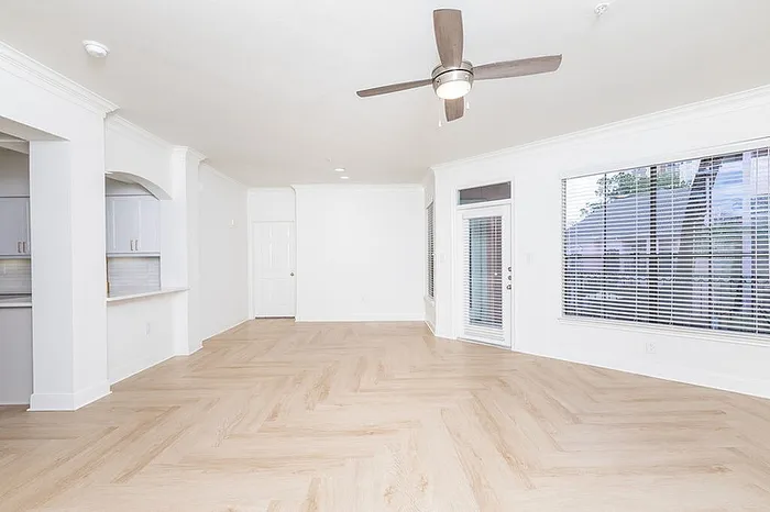 Bright and spacious living area featuring elegant herringbone flooring, modern ceiling fan, and large windows for natural light.