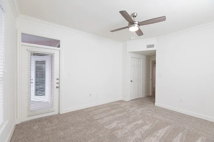 Bright, airy room with elegant carpet flooring, sleek ceiling fan, and access to a private balcony through double glass doors.