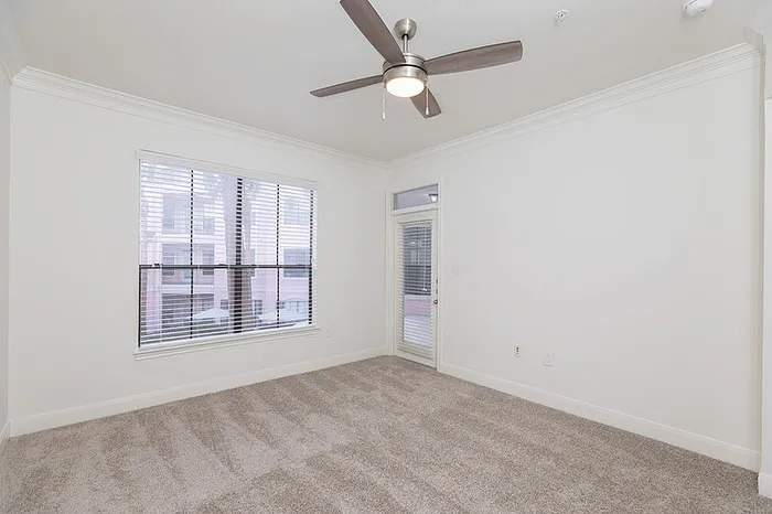 Bright and airy bedroom with plush carpet, large window, ceiling fan, and access to a balcony.