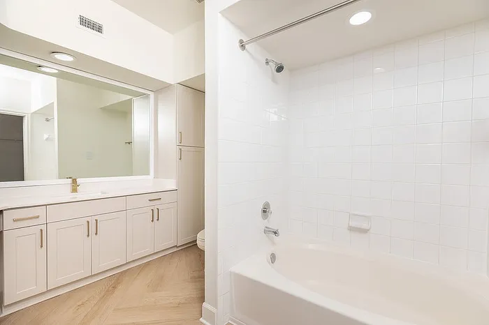 Elegant bathroom with sleek white cabinetry, large mirror, and pristine bathtub, offering a modern and inviting space.