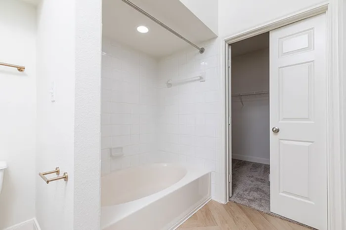 Bright and modern bathroom with a sleek bathtub and a spacious closet, featuring elegant fixtures and stylish tile design.