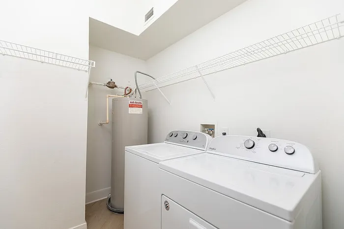 Modern laundry room with white washer and dryer, featuring a spacious water heater and convenient shelving.