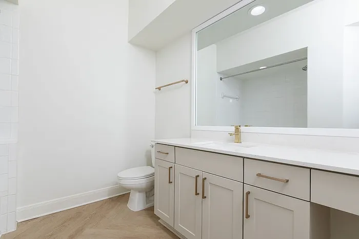 Elegant modern bathroom with sleek white cabinetry, gold fixtures, and a spacious mirror reflecting an inviting atmosphere.