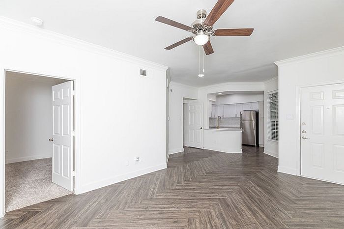 Spacious and modern apartment with open floor plan, featuring elegant wood flooring, a stylish ceiling fan, and a sleek kitchen with stainless steel appliances.