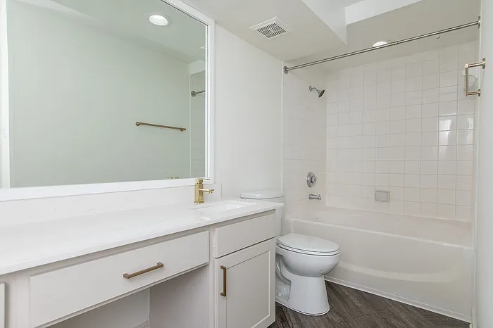 Sleek modern bathroom featuring a spacious vanity with gleaming countertops, elegant gold fixtures, and a pristine tiled bathtub.