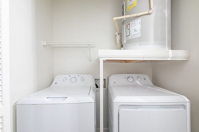 Bright laundry nook featuring modern washer and dryer under an efficient storage shelf.