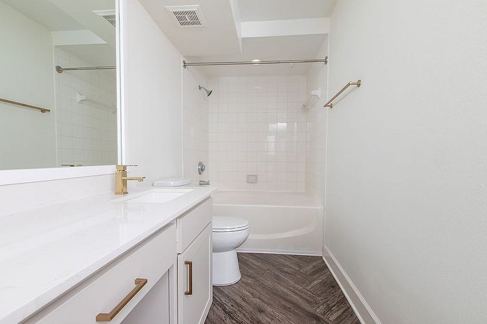 Elegant bathroom with modern fixtures, featuring a pristine white vanity, chic gold accents, and a spacious tub.