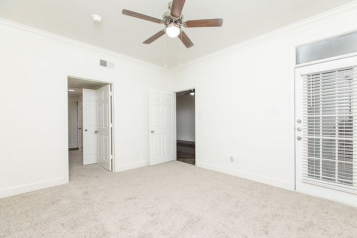 Bright and spacious room with plush carpeting, ceiling fan, and French doors leading to a balcony.