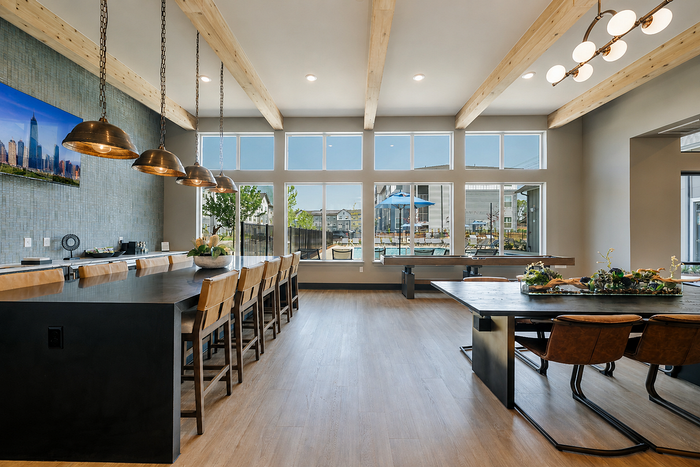 Chic apartment community room with vaulted ceilings, elegant light fixtures, and large windows overlooking a pool area.