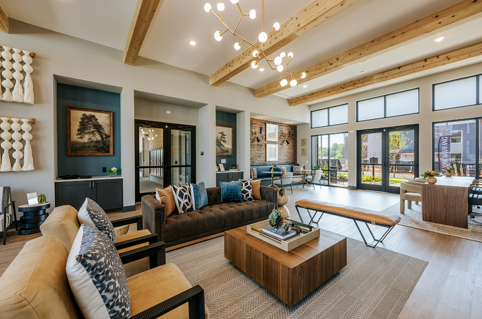Bright and welcoming living area with modern d&eacute;cor, featuring a stylish chandelier, spacious seating, and large windows allowing natural light.