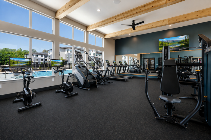 Modern fitness center with large windows showcasing cardio machines, exercise bikes, and strength training equipment overlooking a scenic outdoor pool.