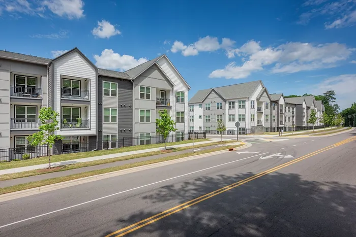 Modern apartment complex with spacious balconies, surrounded by greenery and clear blue skies.