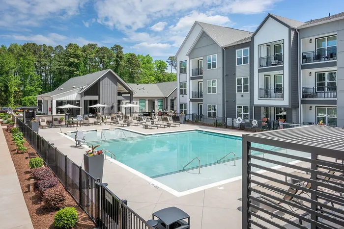 Elegant modern apartment complex with a pristine outdoor swimming pool, surrounded by stylish lounge chairs and lush green landscaping.