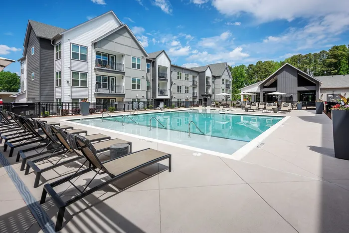 Modern apartment complex with a luxurious outdoor swimming pool, surrounded by sun loungers and well-maintained landscaping, perfect for relaxation and leisure.