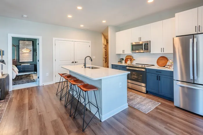 Modern kitchen with sleek stainless steel appliances, a stylish island with bar stools, and a view into the cozy bedroom.
