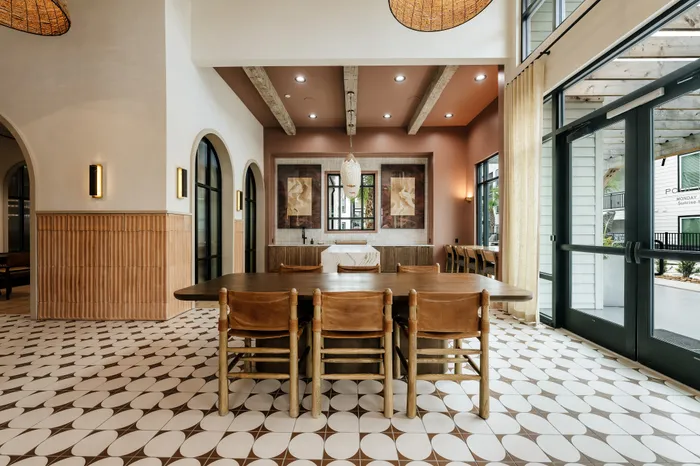 Elegant open-concept dining area with high ceilings, large windows, and chic decor featuring a long wooden table and luxurious leather chairs.