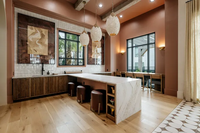 Chic apartment kitchen featuring a stylish island with leather stools, pendant lighting, and large windows offering a serene view. Perfect blend of modern elegance and natural accents.