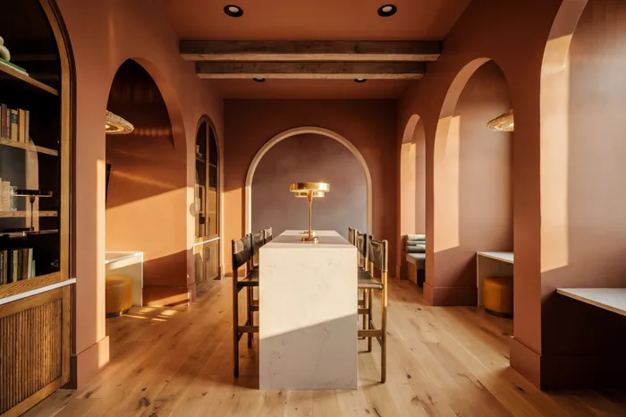 Elegant dining area bathed in warm sunlight, featuring arched doorways, a sleek marble table, and chic leather chairs.